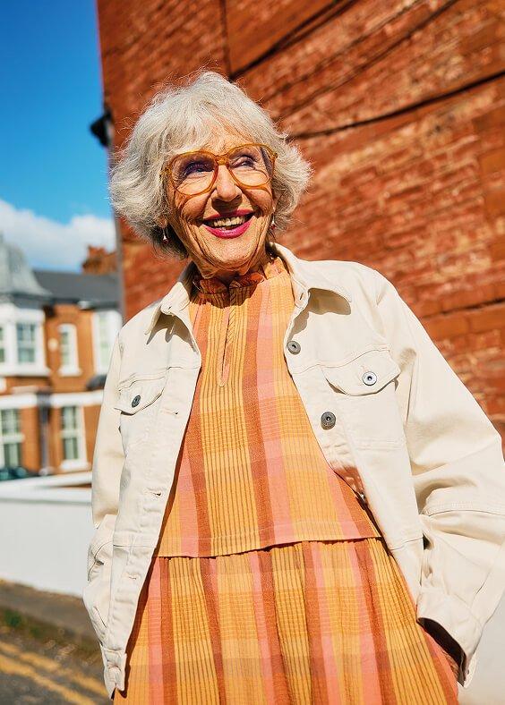 a woman standing on a street corner wearing a dress and jacket